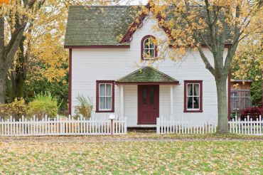 White cottage with burgundy trim and autumn foliage
